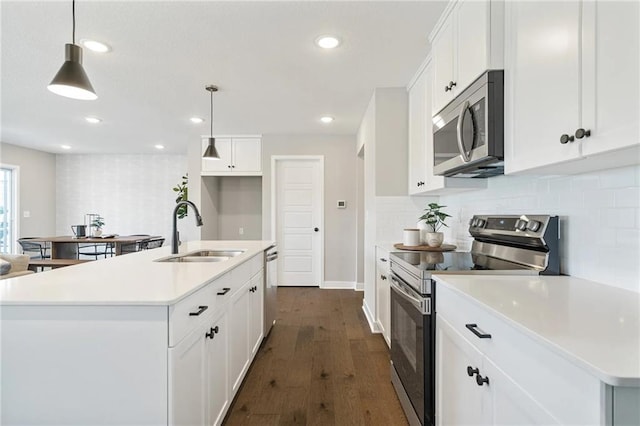 kitchen featuring sink, stainless steel appliances, hanging light fixtures, and a kitchen island with sink