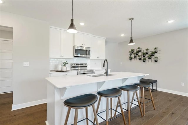 kitchen featuring a kitchen island with sink, sink, stainless steel appliances, and decorative light fixtures