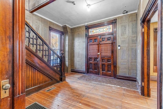 entrance foyer with wood-type flooring, crown molding, and wooden walls