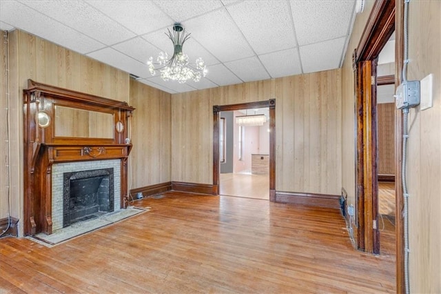 unfurnished living room with a drop ceiling, hardwood / wood-style flooring, and wooden walls