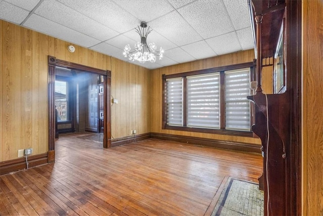 unfurnished room with a notable chandelier, wood walls, a paneled ceiling, and wood-type flooring