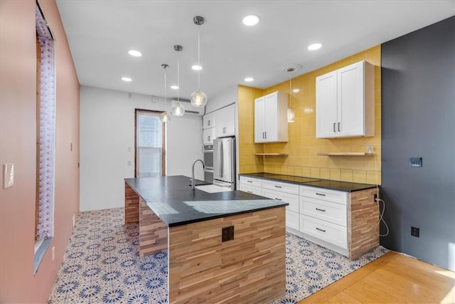 kitchen featuring white cabinets, decorative light fixtures, stainless steel appliances, and a center island with sink