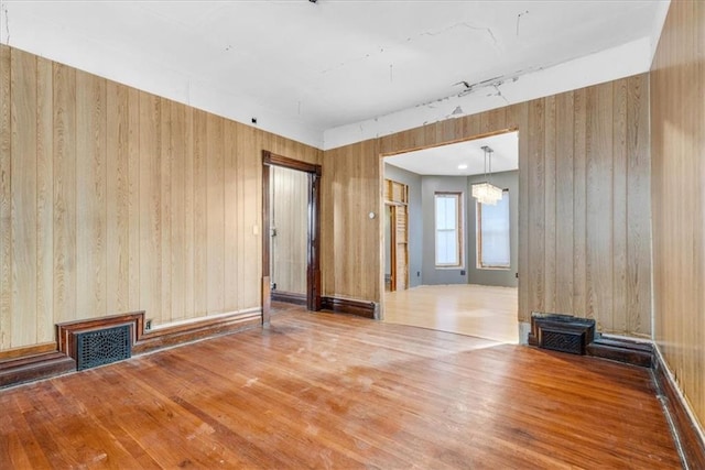 unfurnished living room featuring hardwood / wood-style flooring, wooden walls, and an inviting chandelier