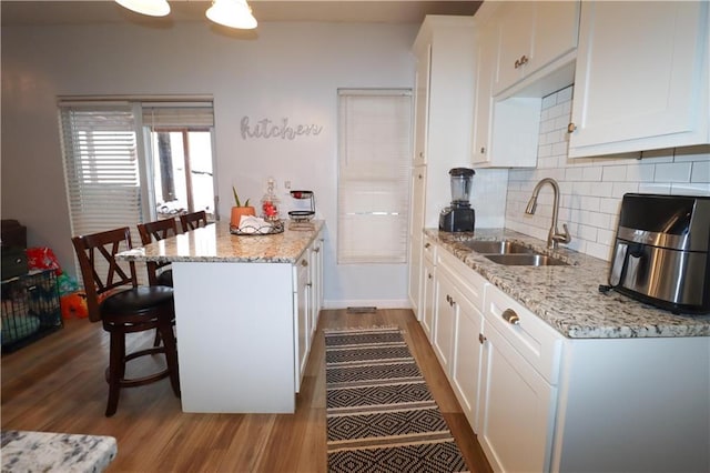 kitchen featuring a kitchen breakfast bar, light stone counters, sink, light hardwood / wood-style floors, and white cabinetry