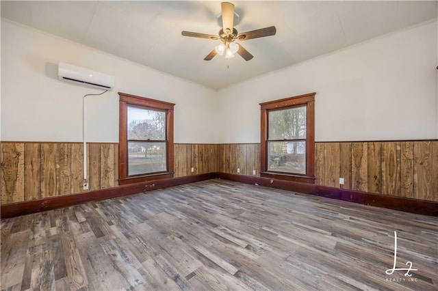 spare room with ceiling fan, wooden walls, a wall mounted air conditioner, and hardwood / wood-style flooring