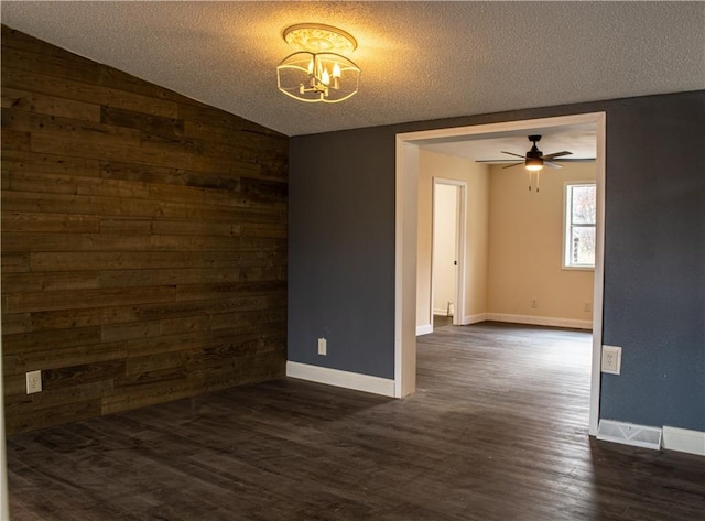 unfurnished room featuring dark hardwood / wood-style flooring, a textured ceiling, vaulted ceiling, wooden walls, and ceiling fan with notable chandelier