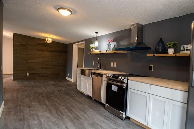 kitchen with appliances with stainless steel finishes, wall chimney exhaust hood, dark wood-type flooring, decorative light fixtures, and white cabinetry