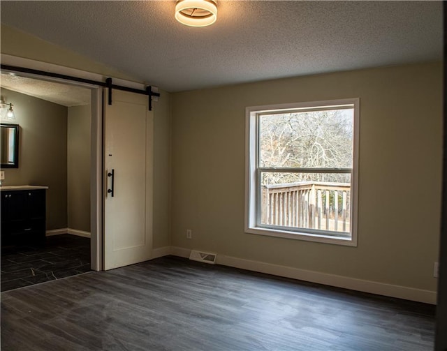 unfurnished bedroom featuring a barn door, dark hardwood / wood-style flooring, and a textured ceiling