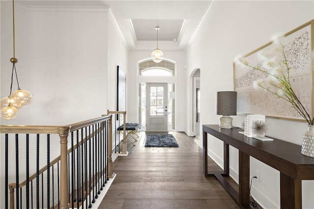 entryway featuring baseboards, ornamental molding, a high ceiling, arched walkways, and wood-type flooring