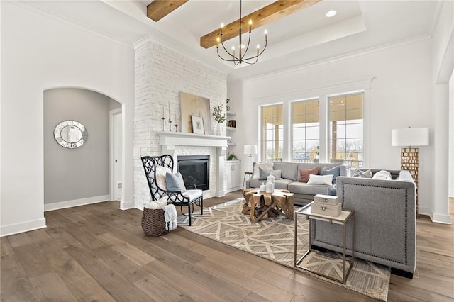 living room with baseboards, beam ceiling, a stone fireplace, an inviting chandelier, and wood finished floors