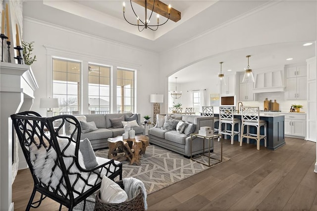 living room with a raised ceiling, arched walkways, dark wood-style flooring, and a chandelier