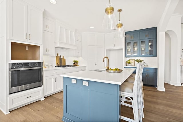 kitchen featuring premium range hood, light wood-style flooring, arched walkways, stainless steel appliances, and a sink