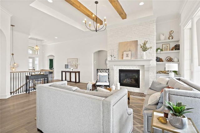 living room with wood finished floors, baseboards, beam ceiling, a fireplace, and arched walkways