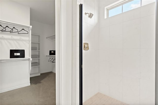 bathroom with a spacious closet, baseboards, and a stall shower