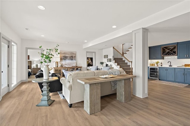 living area with beverage cooler, stairway, light wood-type flooring, recessed lighting, and wet bar