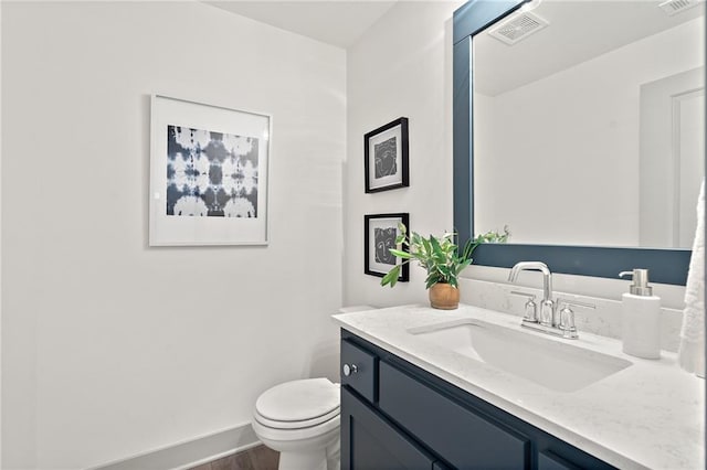 bathroom with vanity, wood finished floors, baseboards, visible vents, and toilet