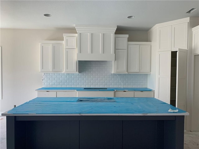 kitchen with tasteful backsplash, white cabinets, a kitchen island, and stovetop