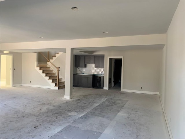 unfurnished living room featuring stairs and baseboards