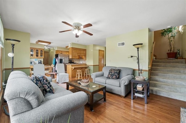 living room featuring stairway, a ceiling fan, visible vents, and light wood-type flooring