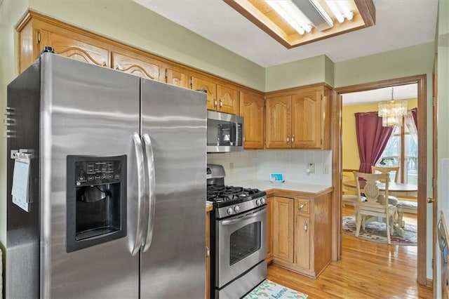 kitchen featuring a chandelier, decorative backsplash, light wood-style flooring, brown cabinets, and stainless steel appliances