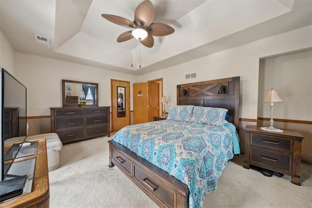 bedroom with a tray ceiling, light colored carpet, visible vents, and ceiling fan