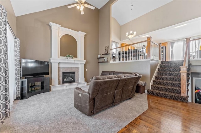 living room with hardwood / wood-style flooring, ceiling fan with notable chandelier, high vaulted ceiling, and a tiled fireplace