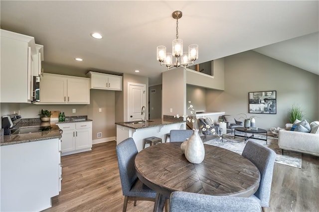 dining room featuring sink, an inviting chandelier, vaulted ceiling, and light wood-type flooring