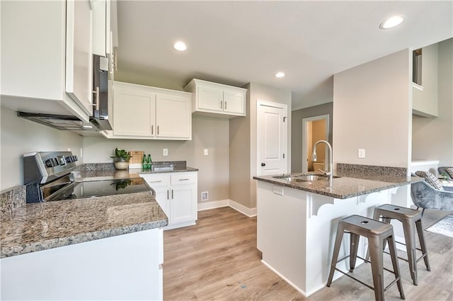 kitchen with light hardwood / wood-style floors, white cabinetry, appliances with stainless steel finishes, and dark stone counters