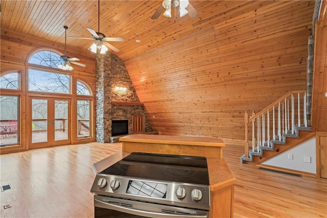 kitchen with light wood-type flooring, high vaulted ceiling, a stone fireplace, and stainless steel electric range