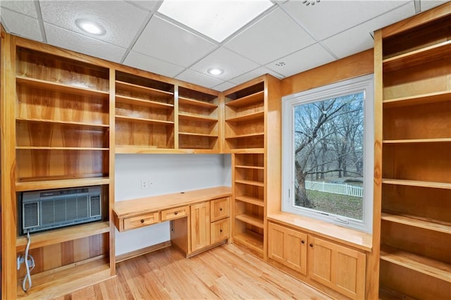 unfurnished office featuring built in desk, light hardwood / wood-style flooring, and a drop ceiling