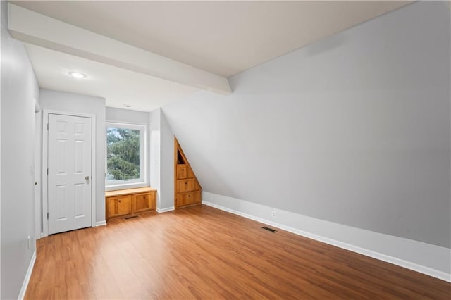 additional living space with light hardwood / wood-style flooring and lofted ceiling with beams