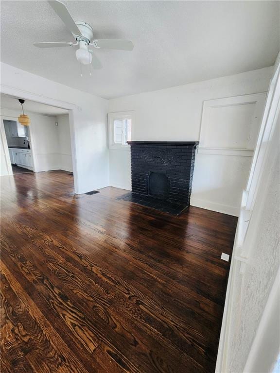 unfurnished living room with a brick fireplace, dark hardwood / wood-style floors, and ceiling fan