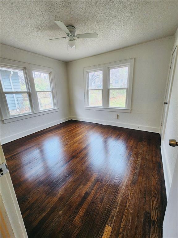 unfurnished room with ceiling fan, dark hardwood / wood-style floors, a wealth of natural light, and a textured ceiling