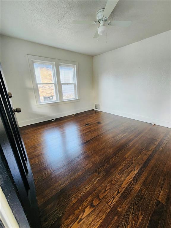 empty room featuring dark hardwood / wood-style flooring, a textured ceiling, and ceiling fan