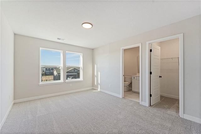 unfurnished bedroom featuring ensuite bath, a spacious closet, a closet, and light carpet