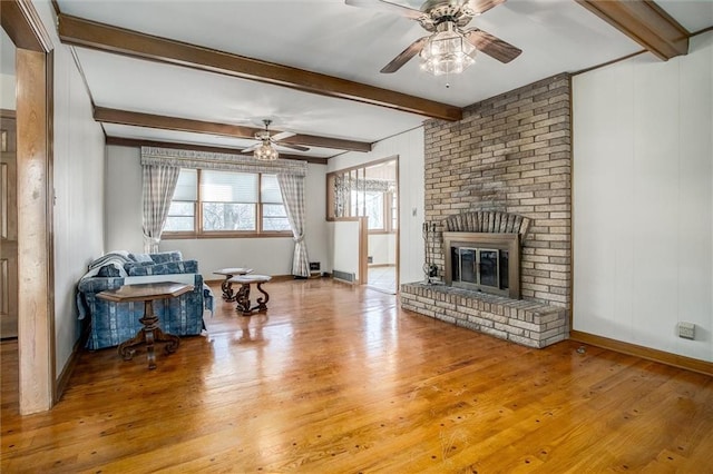 living room with a fireplace, ceiling fan, light hardwood / wood-style flooring, and beamed ceiling