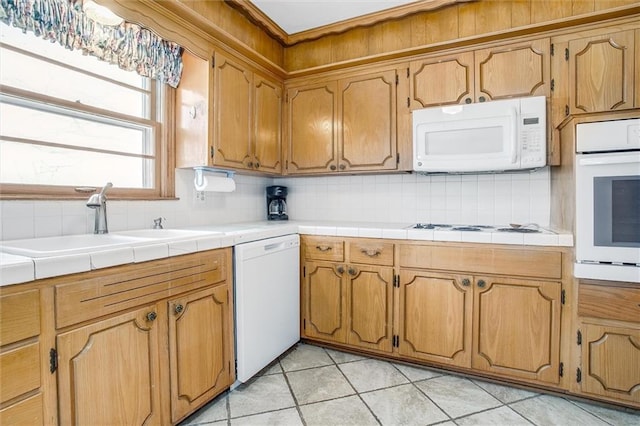 kitchen featuring tasteful backsplash, white appliances, sink, light tile patterned floors, and tile counters