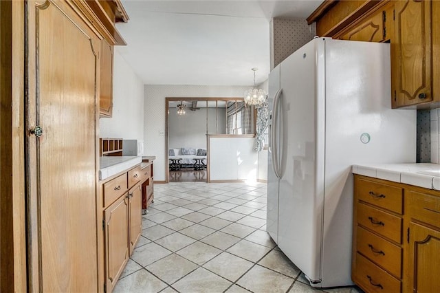 kitchen featuring tile countertops, white fridge with ice dispenser, light tile patterned flooring, and a chandelier