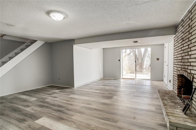 unfurnished living room with hardwood / wood-style floors, a textured ceiling, and a brick fireplace