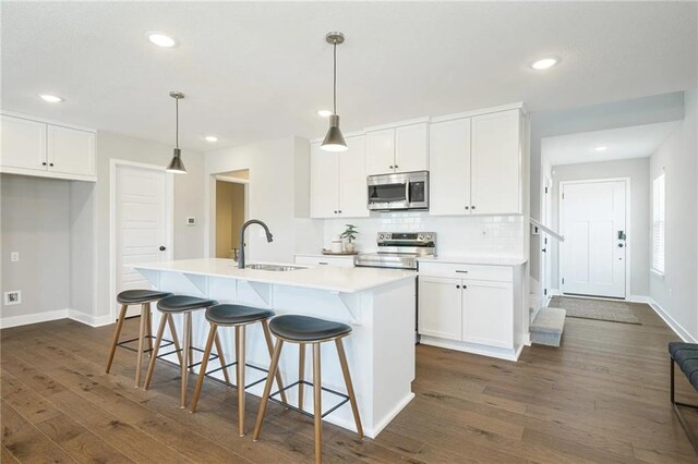 kitchen with decorative light fixtures, a center island with sink, white cabinets, and appliances with stainless steel finishes