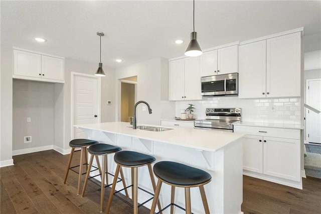 kitchen with sink, appliances with stainless steel finishes, white cabinetry, a center island with sink, and decorative light fixtures