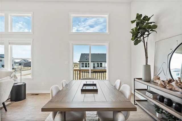 dining area with a towering ceiling, light wood-type flooring, and plenty of natural light