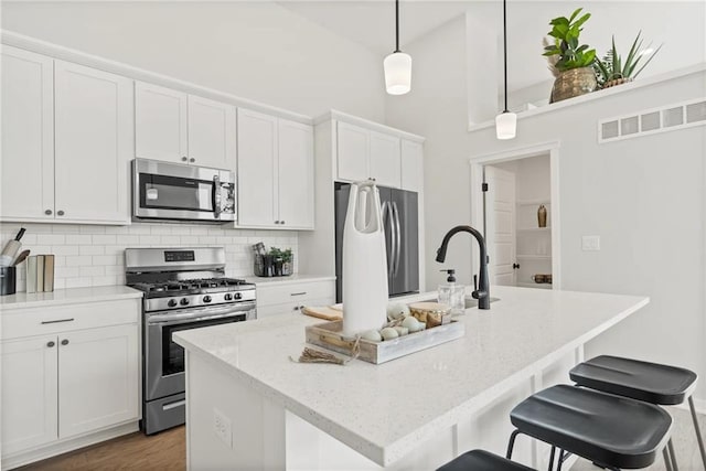 kitchen with pendant lighting, appliances with stainless steel finishes, white cabinetry, light stone counters, and an island with sink