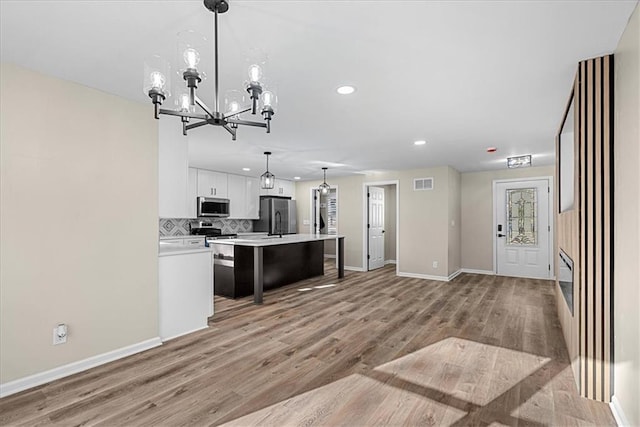 kitchen with a center island, white cabinets, light wood-type flooring, decorative light fixtures, and stainless steel appliances