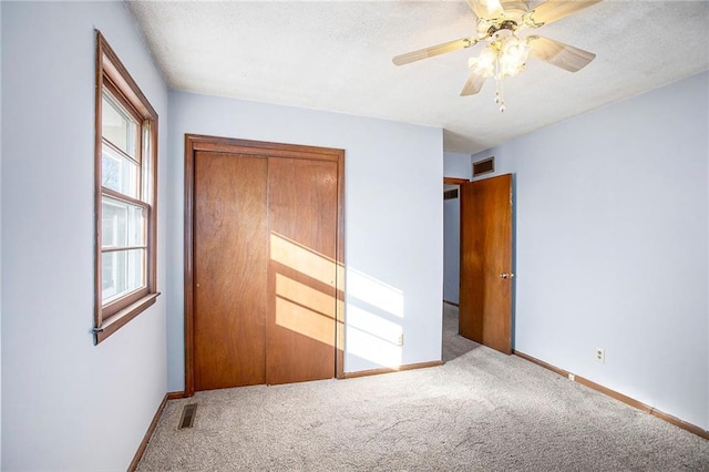 unfurnished bedroom featuring ceiling fan, light colored carpet, a textured ceiling, and a closet