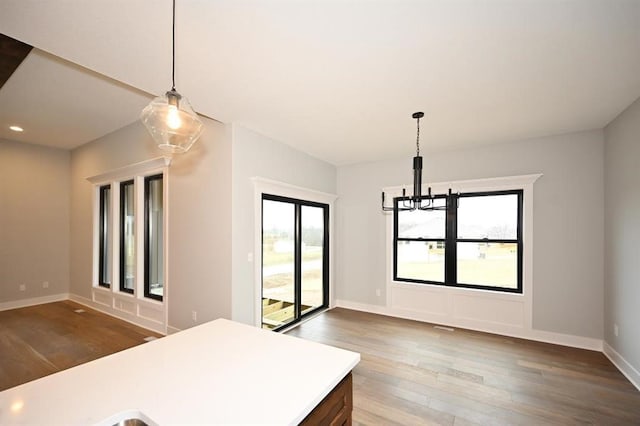 kitchen featuring pendant lighting, wood finished floors, an inviting chandelier, light countertops, and baseboards