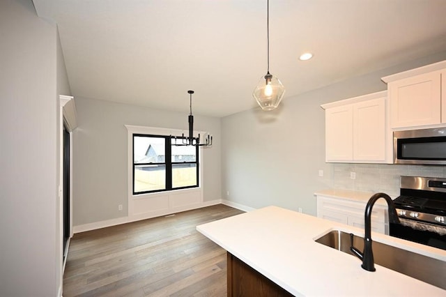 kitchen with stainless steel appliances, hanging light fixtures, light countertops, light wood-style floors, and backsplash