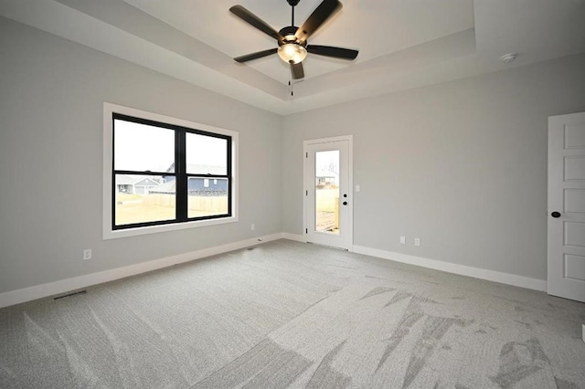 empty room with a tray ceiling, carpet flooring, visible vents, and baseboards