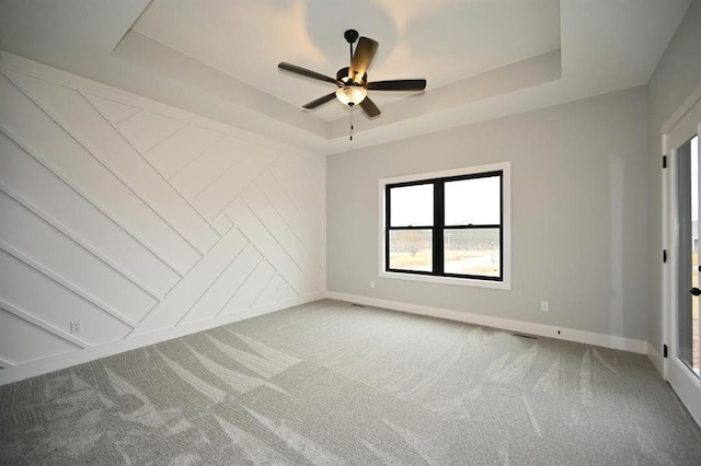 carpeted empty room with a tray ceiling, baseboards, and ceiling fan