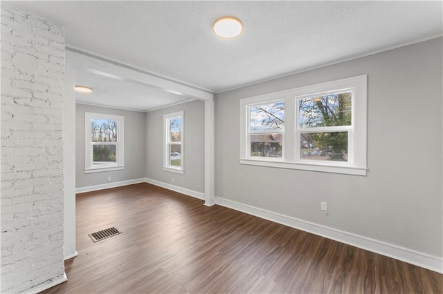 empty room with a textured ceiling, a healthy amount of sunlight, and dark hardwood / wood-style floors